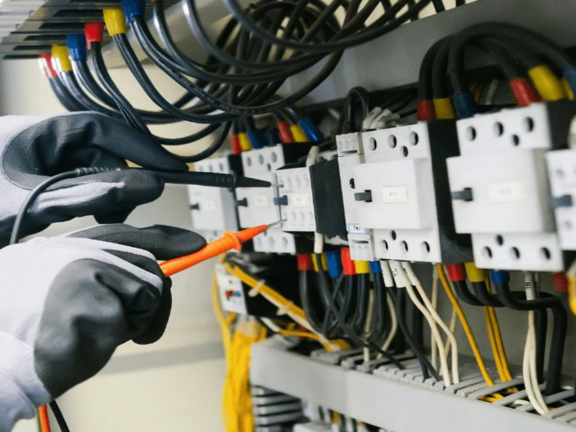 Gloved hands testing a control panel with meter leads
